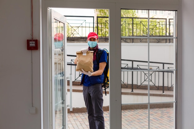 Repartidor de pie con mochila termo amarilla para entrega de alimentos cerca de la entrada a casa con espacio vacío para copiar y pegar