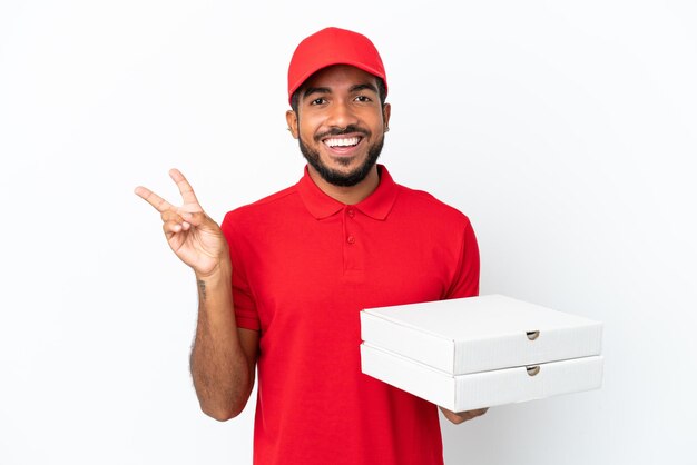 Repartidor de pizza recogiendo cajas de pizza aislado sobre fondo blanco sonriendo y mostrando el signo de la victoria