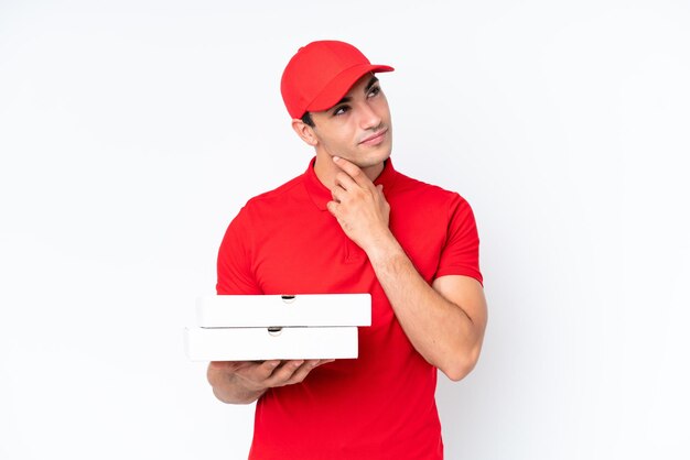 Repartidor de pizzas hombre caucásico con uniforme de trabajo recogiendo cajas de pizza aisladas de fondo blanco mirando hacia un lado y sonriendo