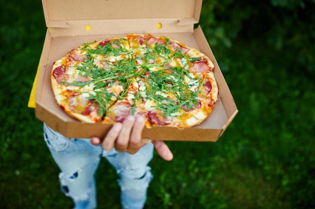 Repartidor de pizzas Mensajero masculino irreconocible entregando pizza en caja abierta del parque Concepto de servicio de entrega de comida rápida