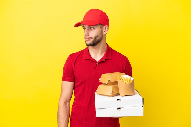 Repartidor de pizzas recogiendo cajas de pizza y hamburguesas sobre fondo aislado mirando hacia el lado