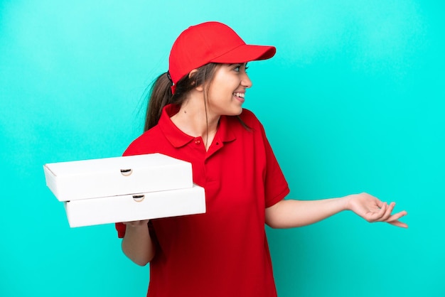 Repartidor de pizzas con uniforme de trabajo recogiendo cajas de pizza aisladas de fondo azul con expresión de sorpresa mientras mira de lado