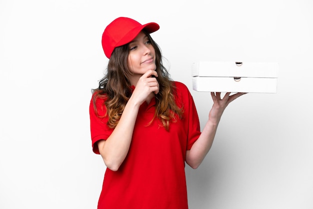 Repartidor de pizzas con uniforme de trabajo recogiendo cajas de pizza aisladas de fondo blanco y mirando hacia arriba
