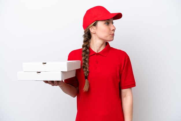 Repartidor de pizzas con uniforme de trabajo recogiendo cajas de pizza aisladas de fondo blanco mirando hacia un lado