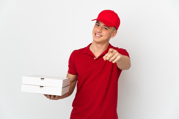 Repartidor de pizzas con uniforme de trabajo recogiendo cajas de pizza aisladas en la pared blanca apuntando hacia el frente con expresión feliz