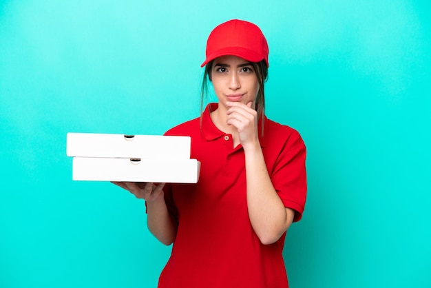 Repartidor de pizzas con uniforme de trabajo recogiendo cajas de pizza aisladas en el pensamiento de fondo azul