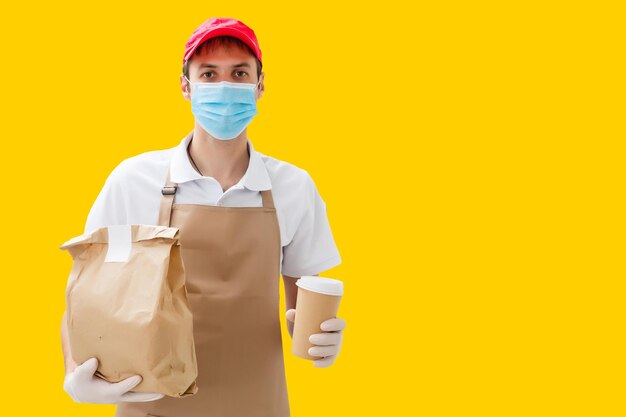 Foto repartidor que lleva una bolsa de papel con productos alimenticios aislados sobre fondo amarillo.