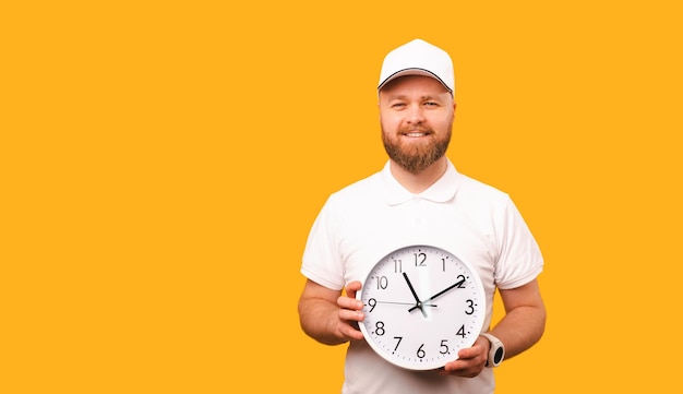 El repartidor sonriente con gorra blanca y camiseta sostiene un reloj redondo