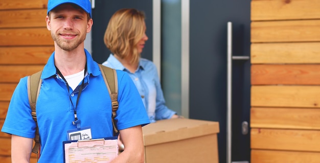 Repartidor sonriente en uniforme azul que entrega la caja del paquete al concepto de servicio de mensajería del destinatario smil