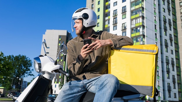 Un repartidor con un teléfono está sentado en un scooter y esperando un pedido Entrega de mensajería