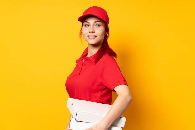 Repartidora de pizza sosteniendo una pizza sobre pared aislada con los brazos cruzados y feliz