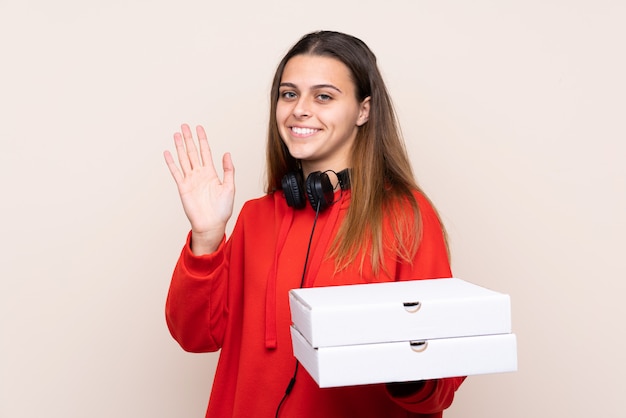 Repartidora de pizza sosteniendo una pizza sobre pared aislada saludando con la mano con expresión feliz
