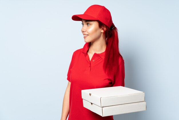 Repartidora de pizza sosteniendo una pizza sobre la pared mirando hacia un lado y sonriendo