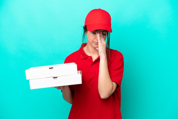 Foto repartidora de pizza con uniforme de trabajo recogiendo cajas de pizza aisladas de fondo azul con expresión cansada y enferma