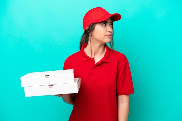 Repartidora de pizzas con uniforme de trabajo recogiendo cajas de pizza aisladas de fondo azul mirando hacia un lado