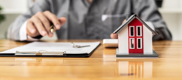 Réplica de una pequeña casa naranja sobre una mesa, un vendedor de un proyecto de vivienda está redactando un contrato de venta para un cliente que reserva una casa en el proyecto que mantiene. Concepto de comercio de bienes raíces