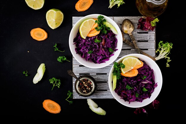 Repolho roxo cozido com cenouras e aipo em uma tigela branca sobre uma mesa preta.