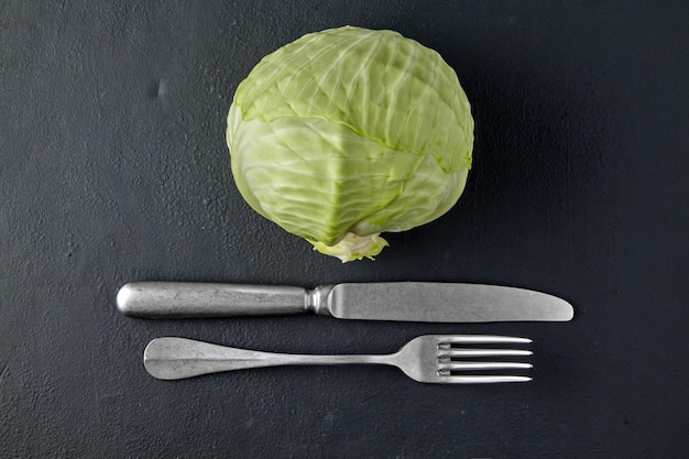 Foto repollo blanco y tenedor con cuchillo en la mesa de hormigón negro