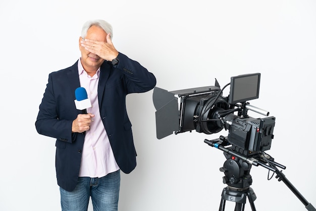 Repórter Brasileiro de meia idade segurando um microfone e relatando notícias isoladas no fundo branco, cobrindo os olhos com as mãos. Não quero ver nada