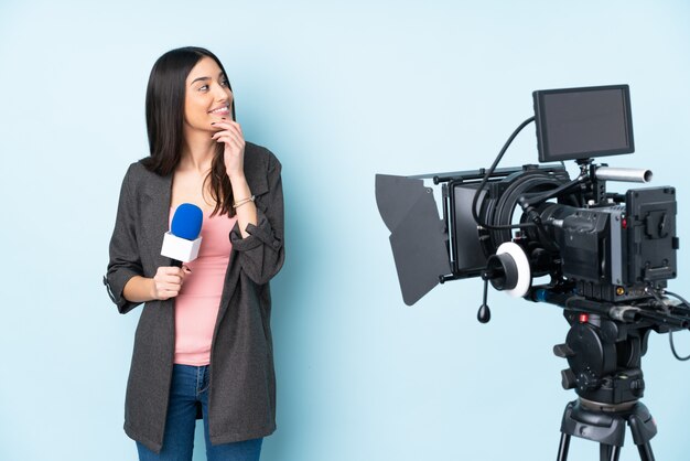 Repórter mulher segurando um microfone e reportando notícias em azul, olhando para o lado