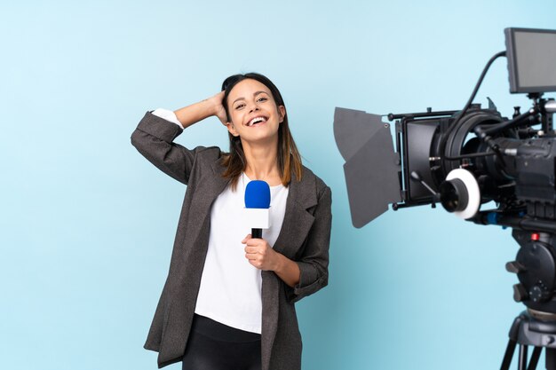 Foto repórter mulher segurando um microfone e reportando notícias sobre parede azul rindo