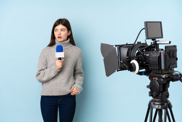 Reporterfrau, die ein Mikrofon hält und Nachrichten über lokalisierter blauer Wand berichtet