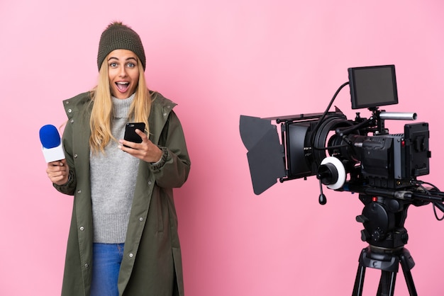 Reporterfrau hält ein Mikrofon und berichtet Nachrichten isoliert rosa Hintergrund überrascht und sendet eine Nachricht