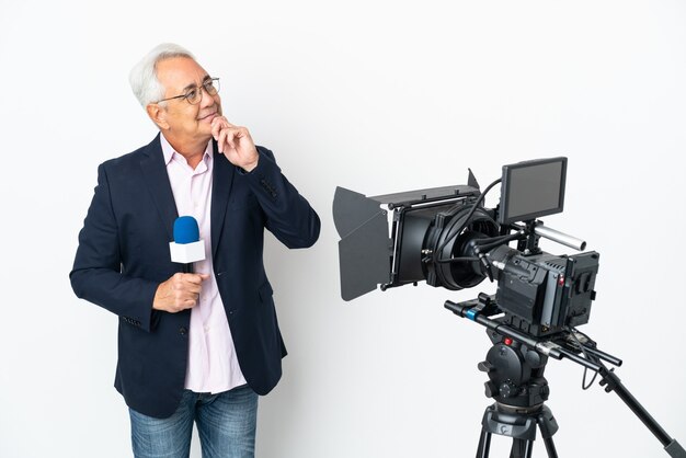 Reportero hombre brasileño de mediana edad sosteniendo un micrófono y reportando noticias aisladas sobre fondo blanco y mirando hacia arriba