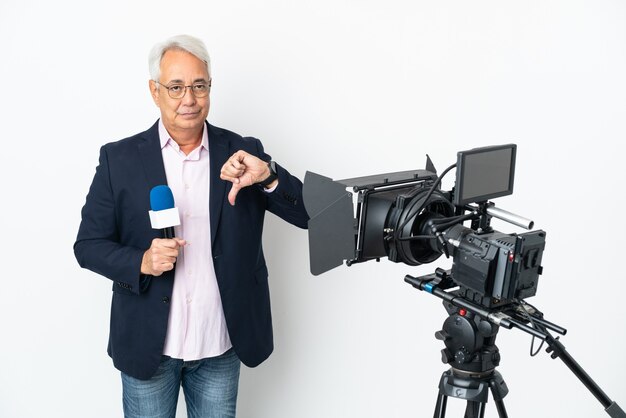 Foto reportero hombre brasileño de mediana edad sosteniendo un micrófono y reportando noticias aisladas sobre fondo blanco mostrando el pulgar hacia abajo con expresión negativa