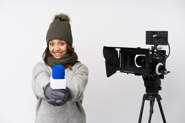 Reportero mujer sosteniendo un micrófono y reportando noticias sobre fondo blanco aislado sosteniendo copyspace imaginario en la palma para insertar un anuncio