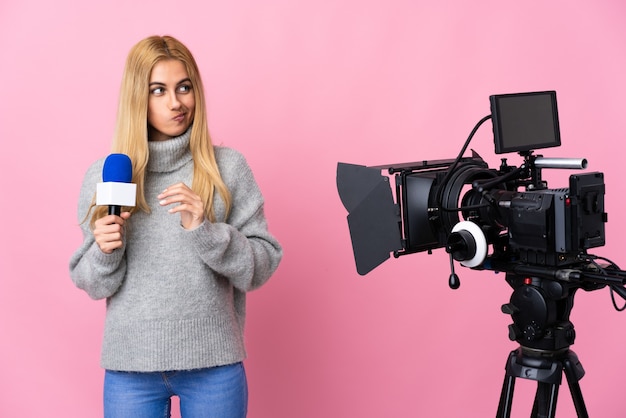Reportero mujer sosteniendo un micrófono y reportando noticias sobre fondo rosa aislado intrigando algo