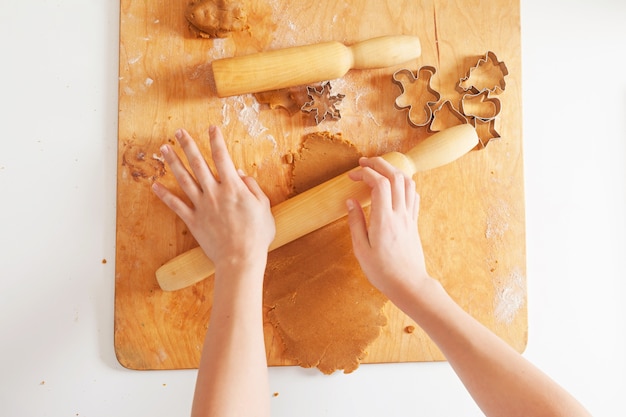 Repostería navideña. Manos de niñas haciendo galletas. Masa de jengibre para pan de jengibre, cortadores de galletas, harina sobre tabla de madera.