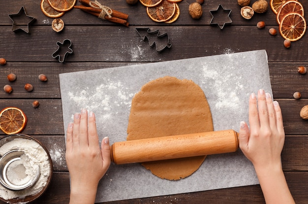 Repostería navideña. Mujer extendiendo masa para galletas de jengibre en la mesa de la cocina, vista superior