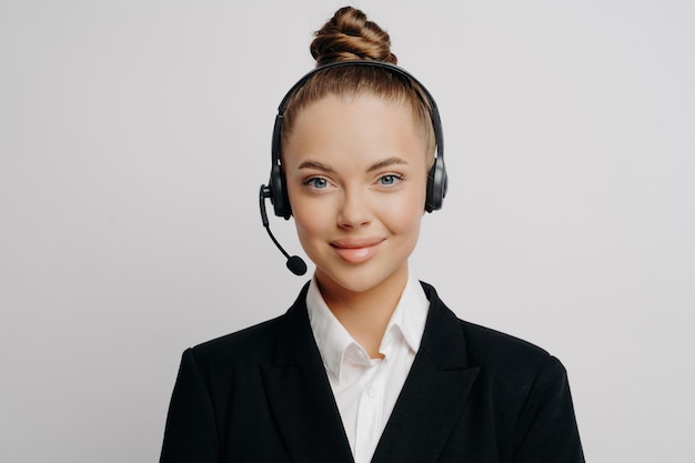 Representante de serviço ao cliente feminino positivo em terno escuro com fone de ouvido sem fio ouve calmamente os clientes sorrindo