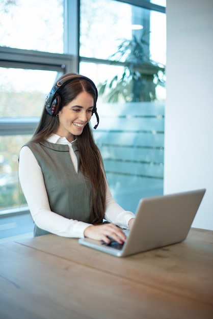 Representante de suporte ao cliente feminino amigável em fone de ouvido com microfone consultando cliente usando laptop no escritório