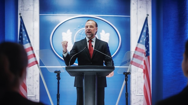 Foto representante de la organización carismática hablando en una conferencia de prensa en el edificio del gobierno oficial de prensa pronunciando un discurso en una cumbre ministro en el congreso con banderas estadounidenses en el fondo