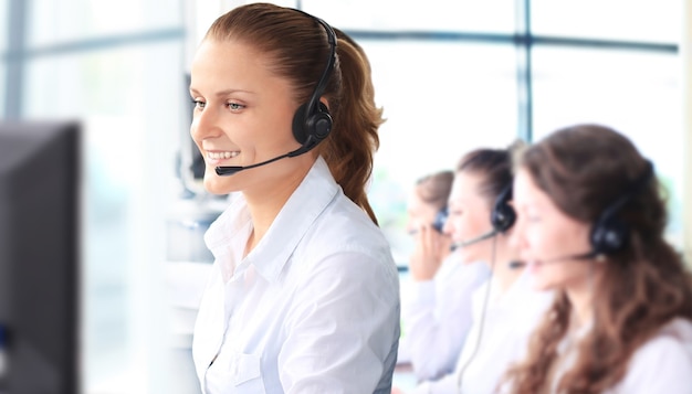 Representante de servicio al cliente mujer sonriente hablando por auriculares con colegas en segundo plano en la oficina