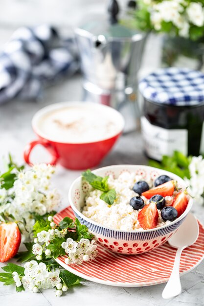 Requesón con bayas, mermelada, fresas frescas y una taza de café con crema para el desayuno.