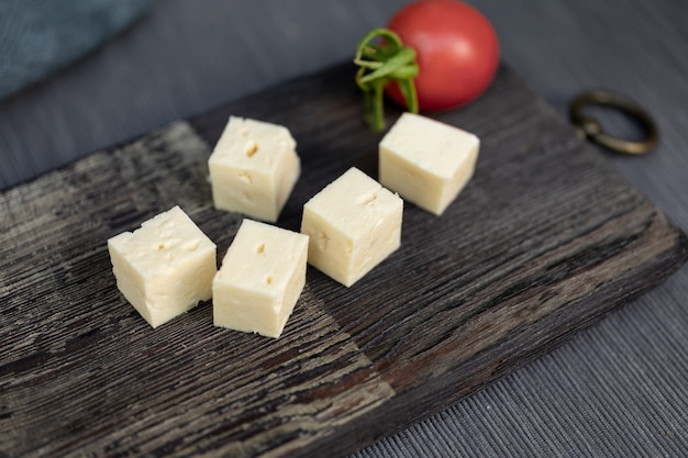 Requesón casero cortado en cubitos sobre una placa de cocina vintage Un tomate en el fondo