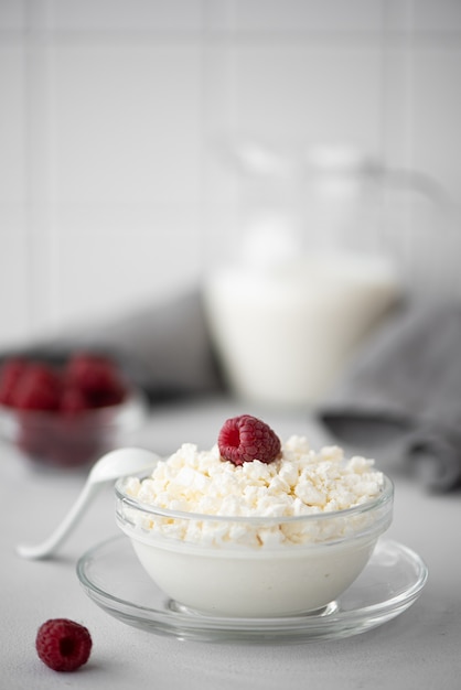 Requesón casero con leche y frambuesas en un recipiente de vidrio sobre una mesa blanca