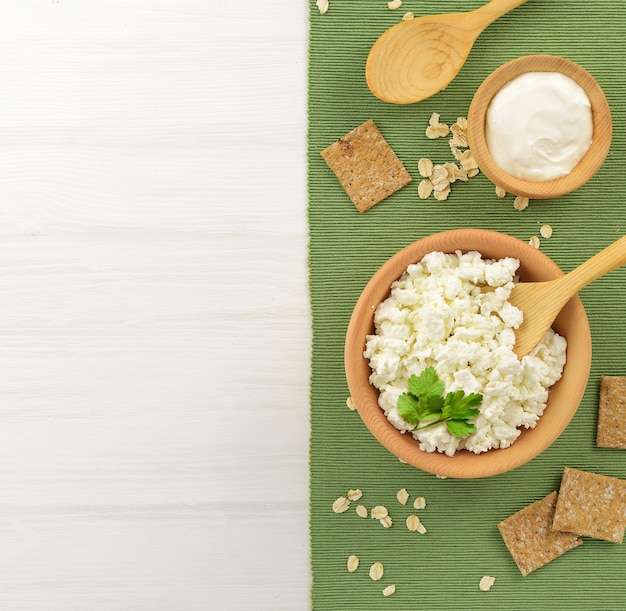 Requesón con crema agria en un cuenco de madera y una cuchara sobre una mesa de madera blanca. Productos lácteos saludables. Copia espacio