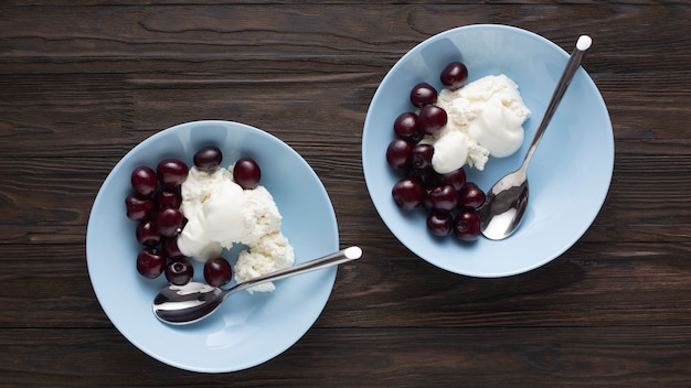 Requesón con delicada crema agria y cerezas maduras en tazones azules sobre una mesa de madera