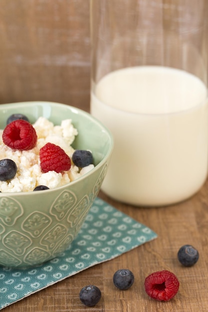 Requesón con frambuesas frescas y arándanos en un bol para un desayuno saludable con bayas maduras y leche en una botella de vidrio