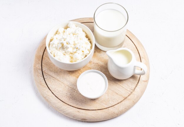 Foto requesón de grano en un recipiente blanco con una jarra de leche sobre un fondo claro