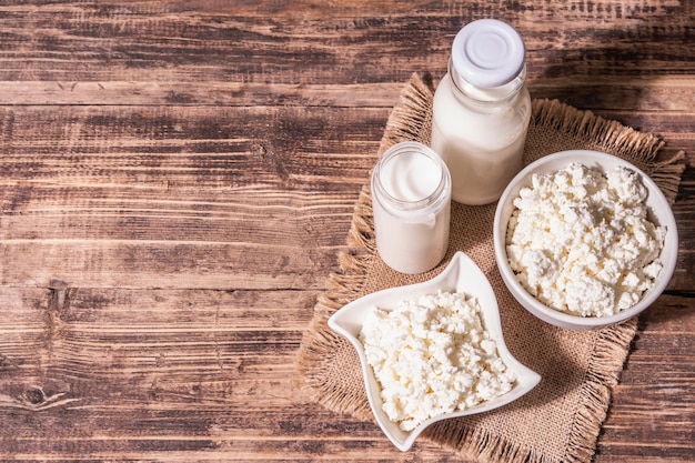 Requesón en un recipiente de cerámica con leche en botellas. Producto lácteo casero en un plato hondo. Mesa de madera vieja, vista superior