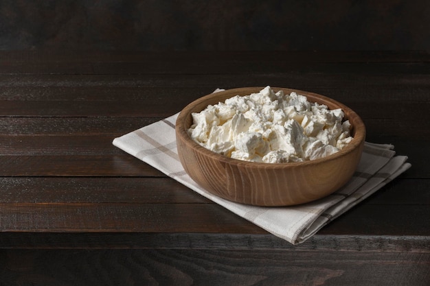 Requesón en un recipiente sobre una mesa de madera antigua. Comida casera de leche saludable. Estilo rústico