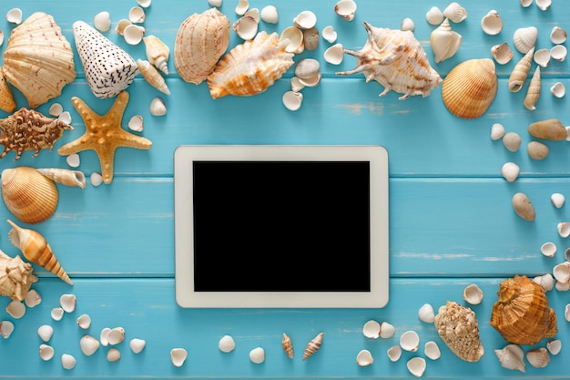 Reserva de boletos en tableta digital con pantalla en blanco, fondo de vacaciones en el mar, conchas marinas en madera azul, maqueta