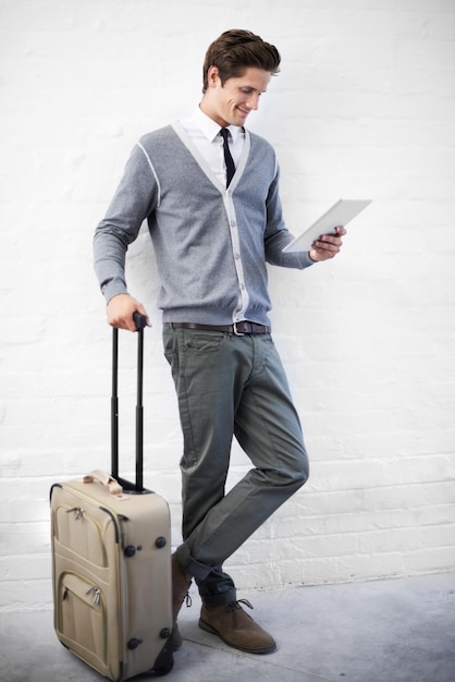 Reservando um voo online Um jovem nerd bonito com bagagem trabalhando em seu tablet