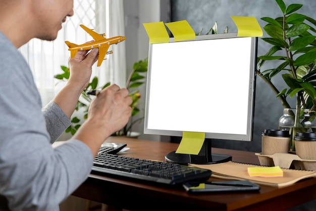 Reserve su recorrido en línea Viajero masculino feliz con modelo de avión que muestra una computadora portátil con pantalla en blanco