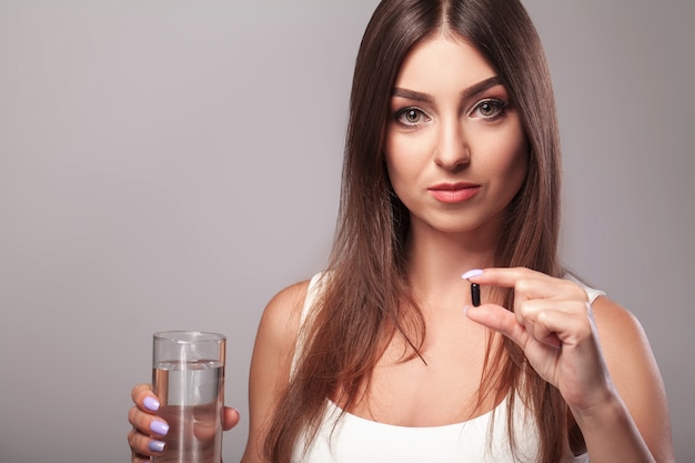 Resfriado y gripe. Mujer sosteniendo un vaso de agua y tomando cápsula